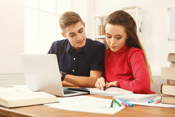 Male and female students at wooden table full of books