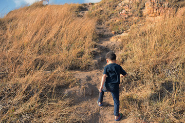 Naklejka na ściany i meble Healthy young boy clinbing and hikking to top of moutain by flipflop. Walking at danger steep hill slope with natural meadow background.