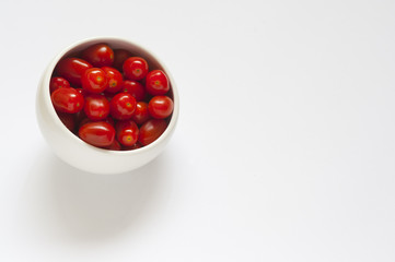 Some red plum tomatoes in a round white bowl on a white background
