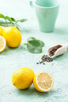 Ripe lemons, tea leaves and a cup on a mint-blue background..