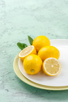 Ripe lemons on a plate on a mint-colored table..