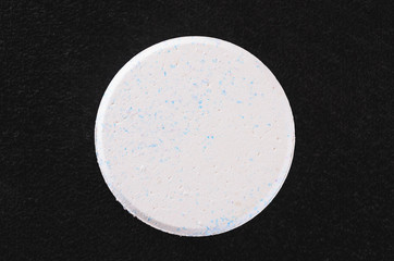 White rounded chlorine tablet isolated on a dark textured background.