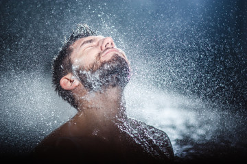 Headshot of a handsome fashionable young man taking shower, with water splashes all over