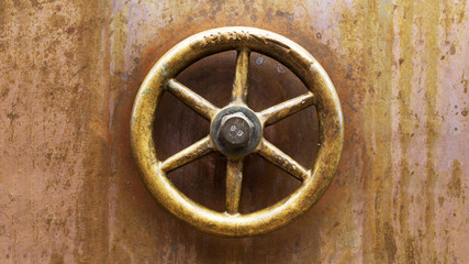 Background of old stained copper metal with a brass valve control knob