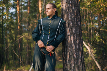 Sexy guy in the woods. In beautiful, old clothes of green color. A medieval man with a copper horn...
