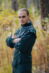 Obraz premium Sexy guy in the woods. In beautiful, old clothes of green color. A medieval man with a copper horn in his hand. Fantasy. Holds a pipe