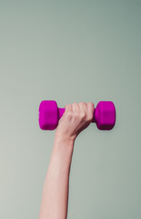 female lifting magenta colored dumbbell against teal background