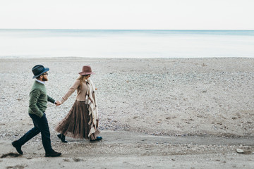 A young and stylish couple is walking on the sea coastline. Romantic date on the beach. Copy space