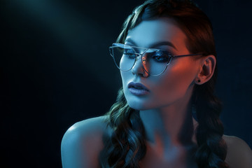 Close up studio portrait of young beautiful sexy woman wearing stylish transparent glasses with metallic frame, posing in blue and red lights. Fashion, beauty, advertising concept. Copy, empty space 