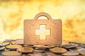 Health Care and money concept. Close up of wooden bag shape with red cross symbol on pile od coins.