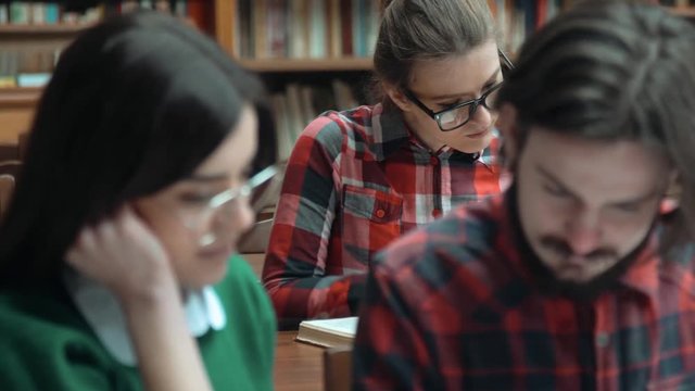 Students reading in library, smart bearded boy turning book pages, intelligent girl in glasses talking to him, concept of pairwork, closeup