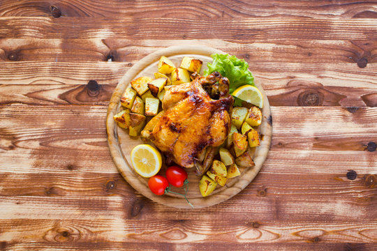 Homemade baked chicken with lemon and potatoes on a wooden background