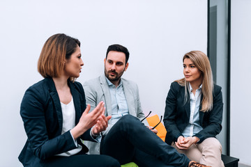 Three collegues talking while sitting in front of white background.
