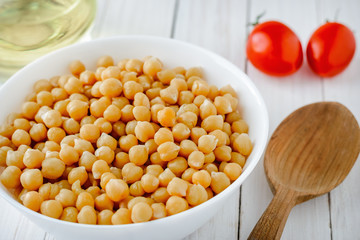 Cooked chickpeas with a plate, tomatoes and olive oil on a wooden table