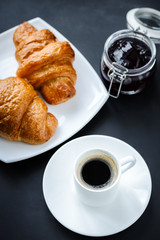 Coffee in a white cup and two croissants with jam 