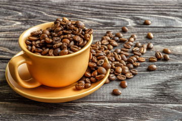 A coffee cup with coffee beans on an old wooden table. Fried coffee beans on a wooden background. Viewing from above.
