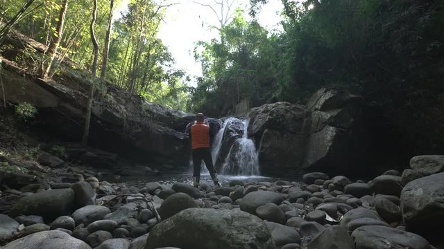traveler alone in a forest use a digital tablet take picture of a waterfall
