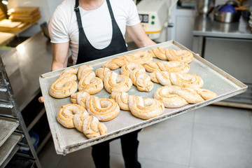 Baker holding a tray with sweet pastry buns at the manufacturing