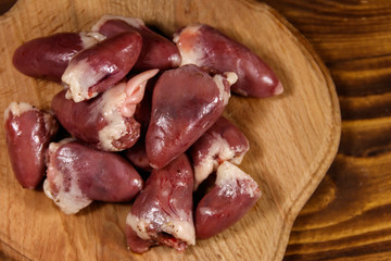 Raw chicken hearts on cutting board on wooden table