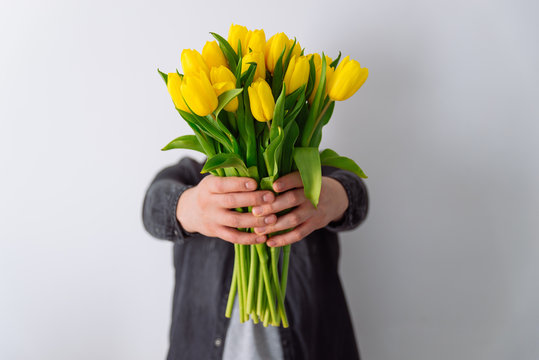 Fototapeta man holds bouquet of yellow tulips in front of him. romantic gift for woman. white background
