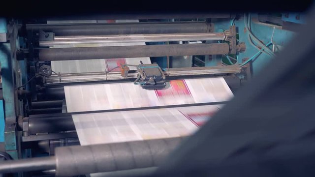 Printed newspapers rolling on printing equipment.