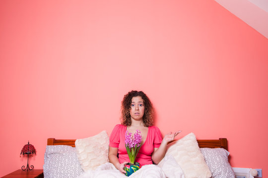 Surprised woman holding flowers in the bed on pink background