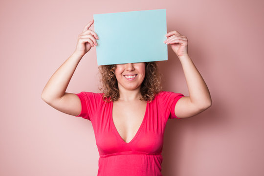 Beautiful curly woman holding empty mint blank board on pink background. Colorful studio portrait.
