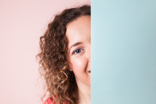 Beautiful curly woman looking behind empty mint blank board on pink background. Colorful studio portrait.