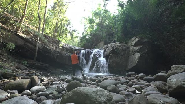 cinemagraph of traveler alone in a forest use a digital tablet take picture of a waterfall