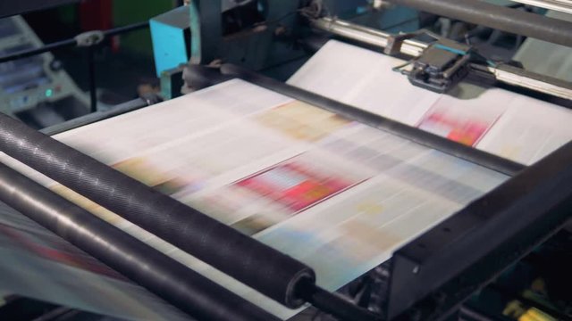 Close-up shot of fresh newspapers rolling on printing equipment.
