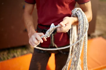 Fototapete Bergsteigen A rock climber tie a knot on a rope. A person is preparing for the ascent. Man learns to tie a knot near climbing wall. Checking the insurance for climbing.  © artiemedvedev