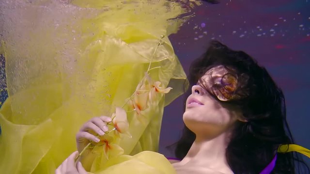 beautiful actress poses under the water with an archide in her hands, on the lady's face is an accessory in the form of a flower