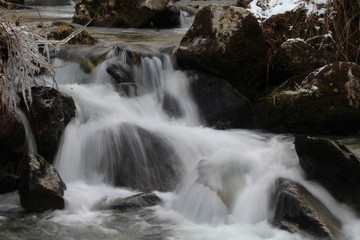 Rivière ou ruisseau de montagne dévalant des rochers en cascade figée par l'hiver et la glace. Branchages congelés. Vitesse lente. 