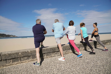 Group of senior people stretching by the beach with coach girl
