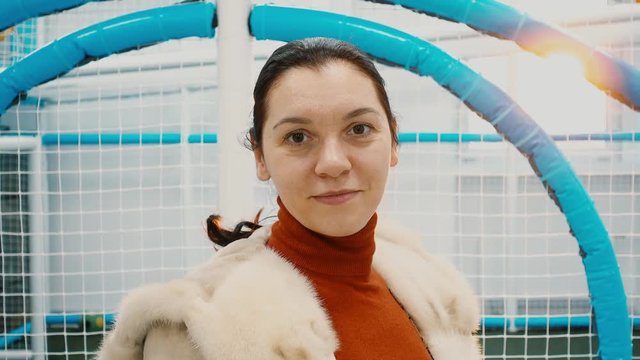 The woman's face in a mink coat against the backdrop of a children's playground. The model of European appearance is 25-30 years old.