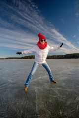 Girl in sunglasse, white jacket, red cap and red scarf walking and having fun on ice on the frozen lake in winter