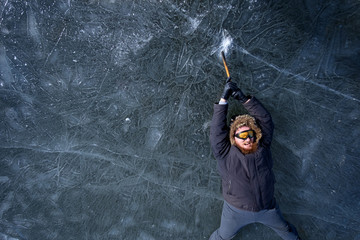 bearded redhead alpinist in protective yellow glasses with ice axe clibing up on icy rock, trying...