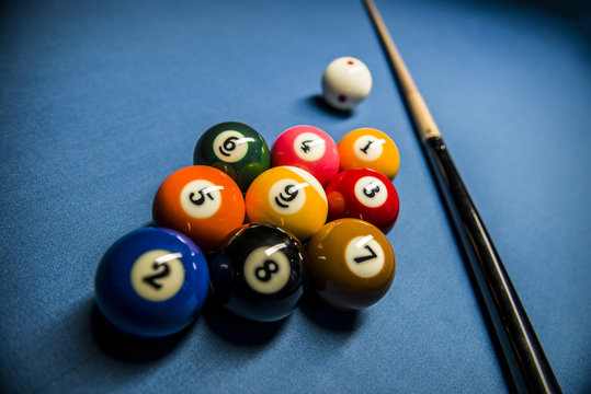 A rack of 9 ball with cue ball and a billiard cue on a blue texture background in a pool club.
