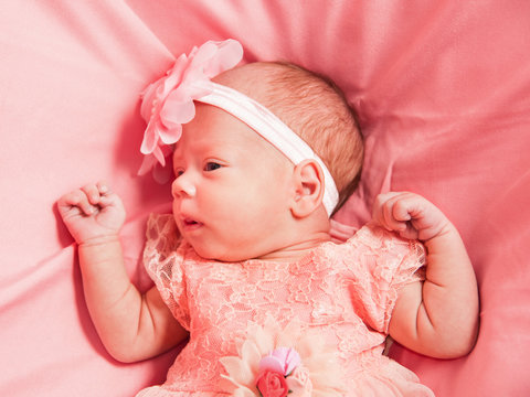 Newborn baby girl in pink dress and hat, lies on pink bed