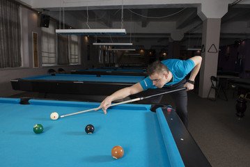 Fototapeta premium Side view of a pool player performing a shot on a ball with chalk on the side of the table.