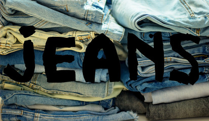 word jeans black  on the background of a stack of multi-colored jeans