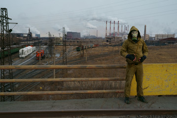 a man in a gas mask on a background of smoky pipes of a factory