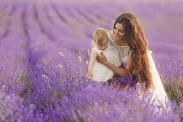 Happy beautiful mother and cute little daughter have fun in aroma lavender fields. Family holiday in summer day.