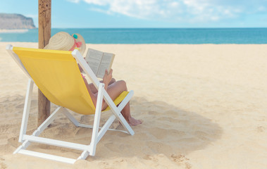 Girl reading a book in sun chair at the beach