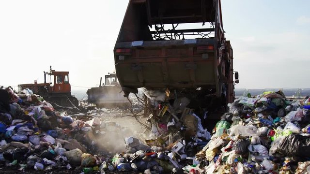 Garbage truck unloads garbage to the dump.Bulldozers work in the background