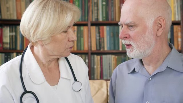 Female professional doctor in white coat with stethoscope at work. Senior woman physician talking to sick senior male patient at home consulting about treatment and therapy options