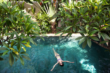 Aerial top view of woman is enjoying relax in swimming pool water among palm and trees from above, tropical vacation holiday concept