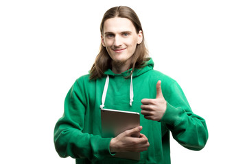 Portrait of young handsome man in green hoodie looking at the camera,
holding digital tablet in one hand and showing okay gesture agains white background. Lifestyle, people and technology concept