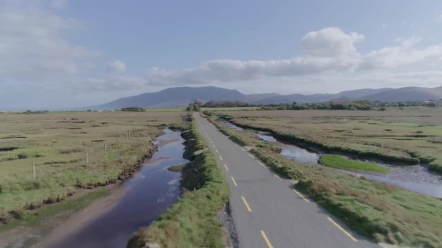 Aerial Footage Of Road Amidst Field Leading Towards Mountain
