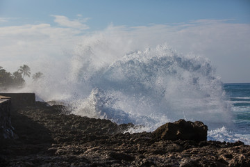 Tropical beach break, ocean wave crushing stone coastline, water splashes